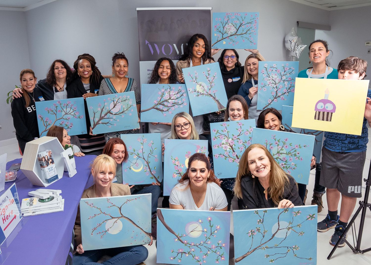 Eighteen women at a Her Becoming gathering in Atlanta, holding the cherry-blossom canvases they painted together